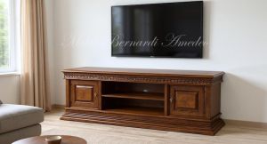 Mobile basso da soggiorno per Tv in legno massiccio con intarsi e intaglio stile classico posizionato in una casa moderna