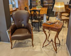 Tavolino quadrato in stile classico in legno di noce intarsiato affiancato ad una poltrona imbottita in vera pelle marrone